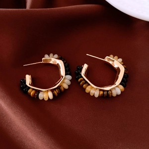 Macro shot of 18K gold plated C-shaped hoop earrings with tiger eye beads on silk