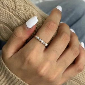Detailed close-up of a gold ring featuring three white pearls and two cubic zirconia