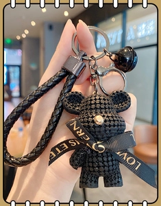 Detail of a black resin bear keychain with woven strap and a small bell decoration