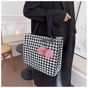Detail of black and white houndstooth tote bag with pink cherry fur pompom accessory