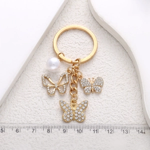Golden butterfly keychain with rhinestones and pearl detail shown against a ruler