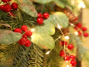 Close-up of Christmas wreath with red berries, pine needles and warm LED light glow