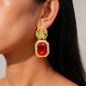 Macro shot of gold leaf earrings featuring a large emerald-cut ruby-red gemstone detail