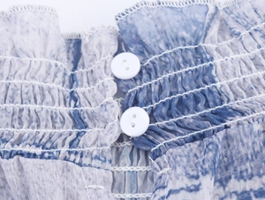 Détail du mousseline tie-dye bleu avec texture smockée et boutons blancs ronds