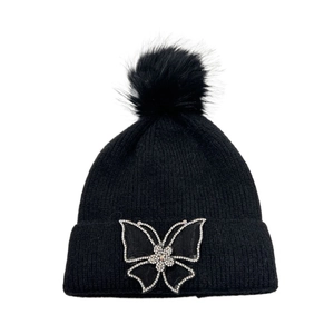 Close-up of black knit beanie featuring a fluffy pompom and rhinestone butterfly detail