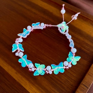 Elegant beaded bracelet with teal butterfly charms and pearls on a wooden display tray