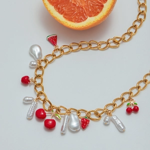 Gold chain necklace with red cherry pendants and pearls on a light grey background