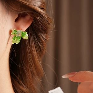 Close-up of a green leaf-shaped earring with gold plating and a sparkling crystal center