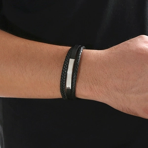 Close-up of layered black leather braided bracelet with engraved silver metal bar detail