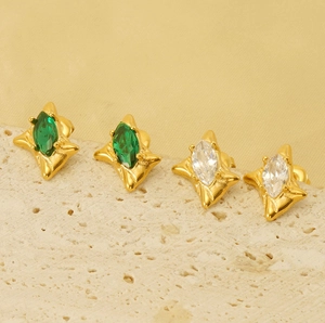 Close-up of emerald and clear marquise zircon earrings on a textured stone surface