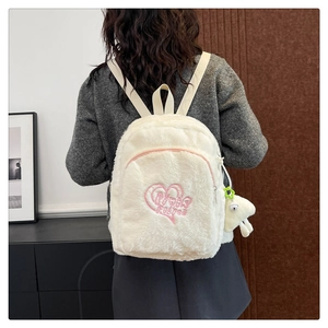 Dettaglio di uno zaino in peluche bianco con ricamo a cuore rosa e ciondolo a forma di animale