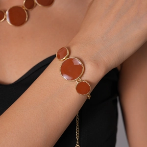 Détail d'un bracelet en émail terracotta rond avec bord perlé doré porté au poignet