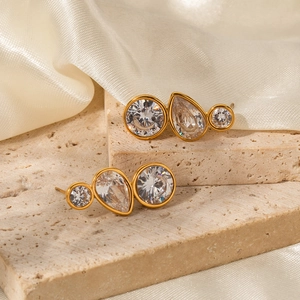 Clous d'oreilles dorés avec trois zircons blancs étincelants sur pierre beige neutre
