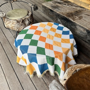 Close-up of vibrant checkerboard outdoor blanket with decorative fringe on wood floor