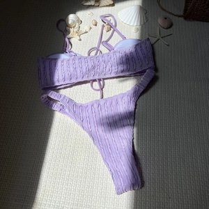 Detail eines lavendelfarbenen strukturierten Bikinisets mit Muscheln auf weißem Stoff
