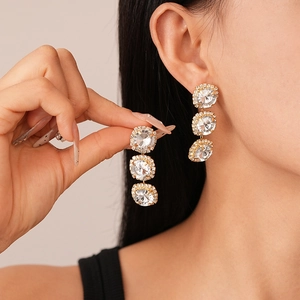 Detail of luxury gold earrings with three dangling round rhinestones worn by a model