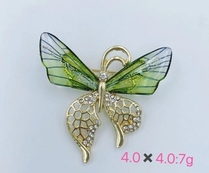 Detail view of a 4x4cm golden butterfly brooch with green wings and white rhinestones