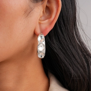 Close-up of silver C-shaped earrings with three graduated crystals on polished metal