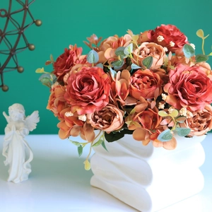 Detailed view of orange silk roses and eucalyptus in a white ceramic wavy vase