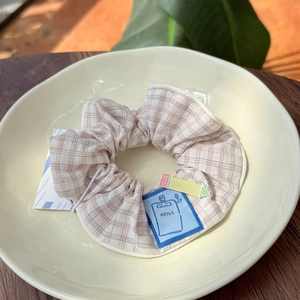 Detailed shot of a beige plaid fabric scrunchie with a blue Notes label in a ceramic bowl