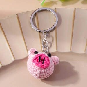 Handmade pink crochet pig keychain with silver metal ring on a cream display board