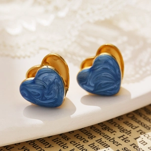 Gros plan de boucles d'oreilles cœur dorées avec émail marbré bleu sur fond vintage