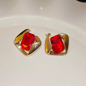 Dettaglio macro di orecchini dorati con pietre rosse quadrate su vassoio in ceramica