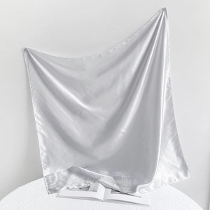 Close-up of a silver satin square scarf with a glossy finish draped over a magazine
