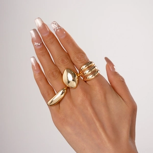 Close-up of golden oval bean and triple-layered minimalist stacking rings on hand