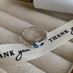 Close-up of silver adjustable ring featuring two square blue stones on a silk ribbon
