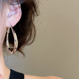 Detail of large twisted silver hoop earring with mirror finish on female model