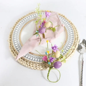 Macro detail of Easter napkin ring with purple faux flowers and spotted eggs on pink linen