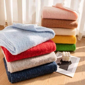Stack of colorful wool scarves in pastel and warm tones on a minimalist wooden floor