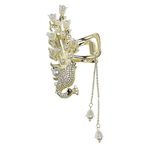 Detail of peacock hair claw clip with golden lilies, pearls, and long tassel chains