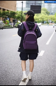 Street style view of a purple nylon backpack with MUMU lettering and black zipper detail