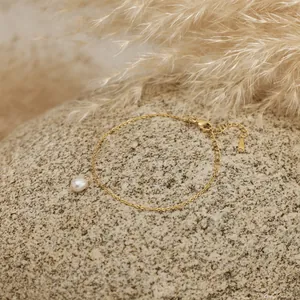 Detail of an 18K gold plated stainless steel chain bracelet with a teardrop pearl charm