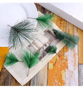 Close-up of six green artificial pine needles and bottle brush branches on a rustic wooden table