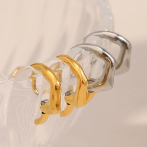 Detailed view of irregular wavy 18K gold and silver hoop earrings on a glass bowl