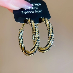 Detailed macro view of spiral gold hoops with black and clear crystals on a black card