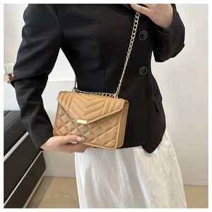 Model showing beige quilted crossbody bag with gold chain strap on shoulder
