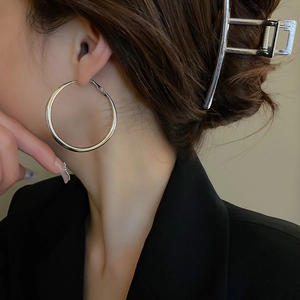 Side view of a model wearing large silver metal hoop earrings with a minimalist design