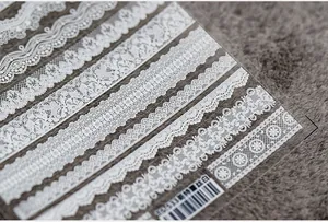 Détail macro de stickers ongles dentelle 5D blanche avec motifs floraux sur fond de velours