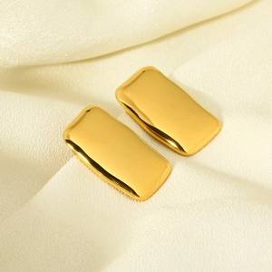 Macro view of polished 18K gold plated rectangular earrings on a silk fabric background