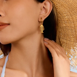 Golden fishbone charm hoop earrings for women worn by a model in a summer beach style