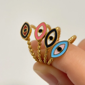 Set mit vier farbenfrohen Evil Eye Emaille-Ringen mit goldenen Perlenbändern an Fingern