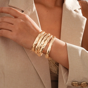 Détail d'un lot de 5 bracelets dorés à texture martelée portés avec un blazer beige
