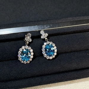 Macro detail of oval aquamarine silver stud earrings with diamond halo in a black gift box