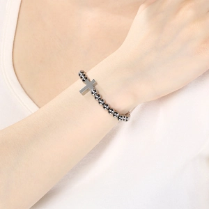 Close-up of minimalist stainless steel beaded bracelet with cross pendant on female wrist