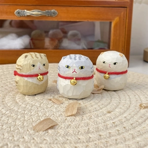 Three handcrafted wooden-style cat figurines with red bell collars on a woven mat