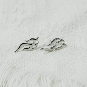 Detailed macro shot of flame-shaped stainless steel earrings on white fabric background